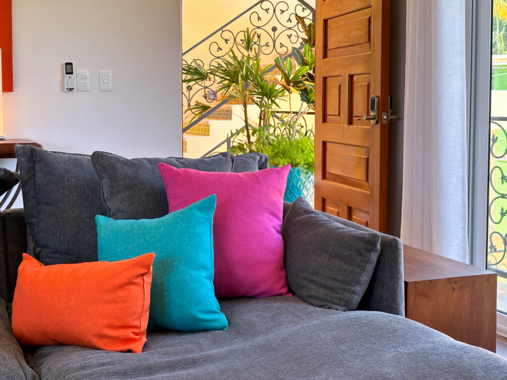 Orange, turquoise, and pink cushions arranged on a gray sofa beside the entrance.