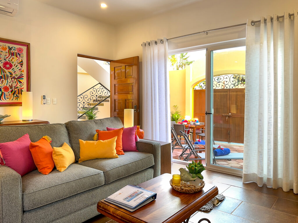 Gray sofa with bright cushions and a wooden coffee table beside glass doors opening onto the patio.
