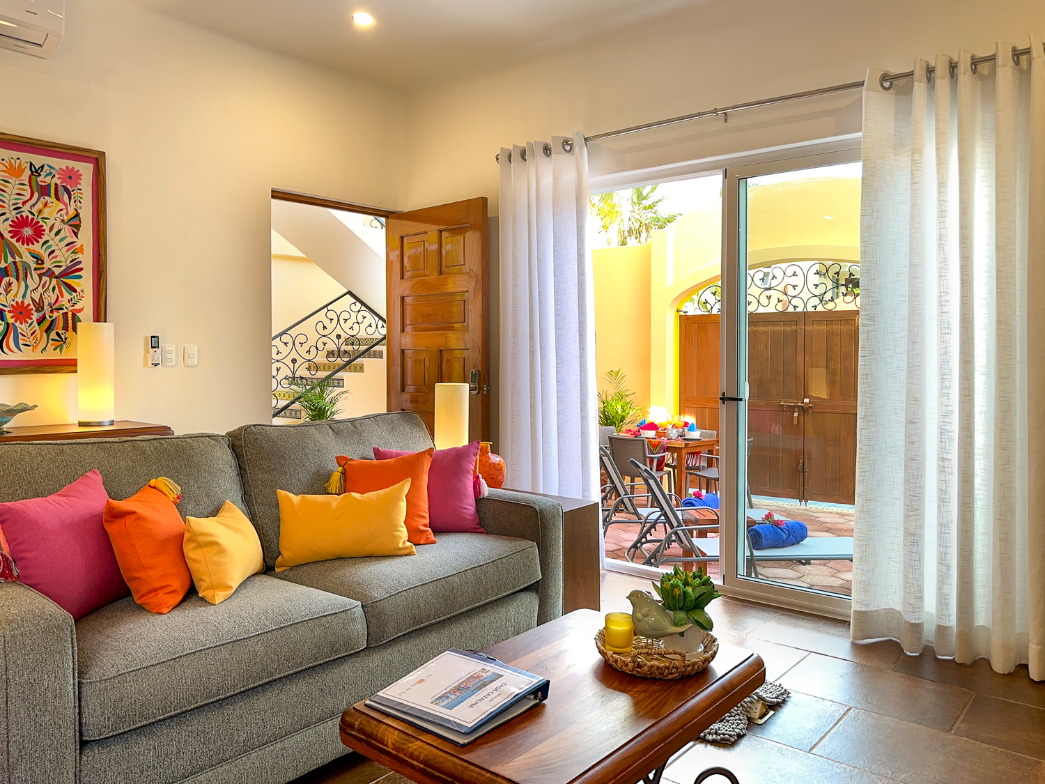 Gray sofa with bright cushions and a wooden coffee table beside glass doors opening onto the patio.