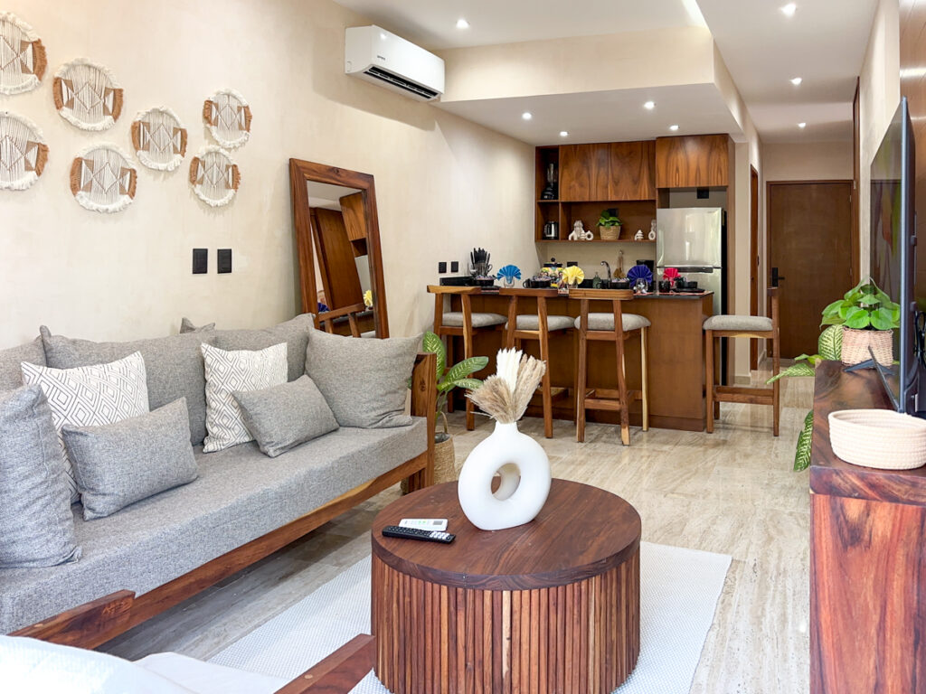 Gray sofa beside a round wooden table, with the kitchen breakfast bar in the background.