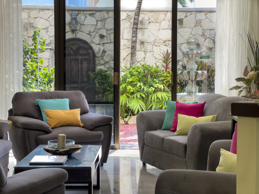 Gray chairs and sofas around a glass coffee table beside doors overlooking a stone-walled garden.