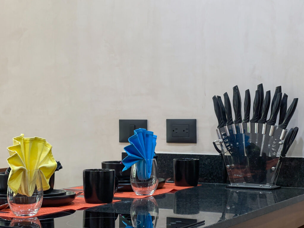 Black dishes, bright folded napkins, and a knife block on a polished dark kitchen counter.