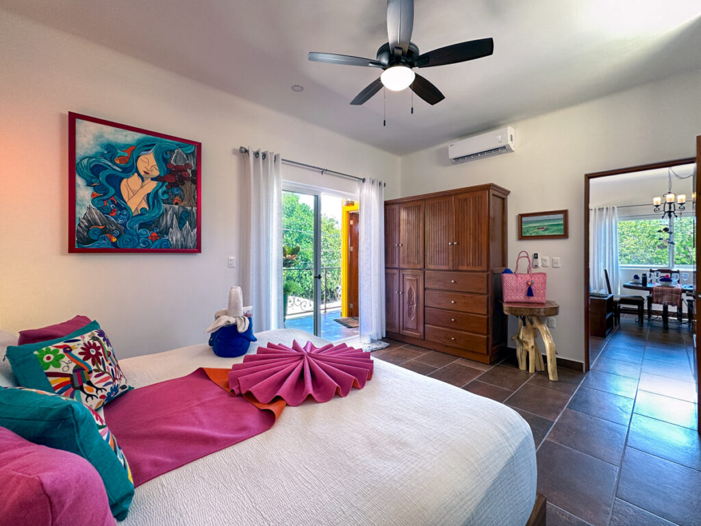 Bedroom with pink bedding accents, framed artwork, wooden wardrobe, and balcony doors.