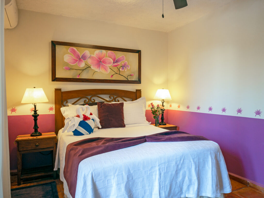Bed beneath pink floral artwork between matching lamps, with a purple accent band along the wall.