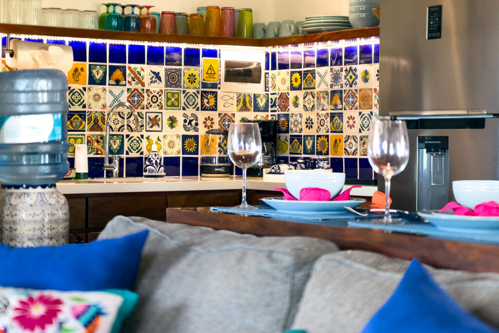 Breakfast bar set with dishes and wine glasses in front of a kitchen with a colorful tile backsplash.