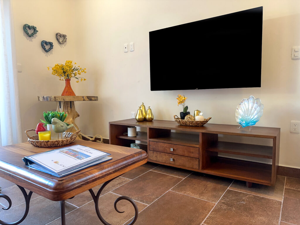 Wall-mounted television above a wooden console, with a coffee table and decorative objects in front.