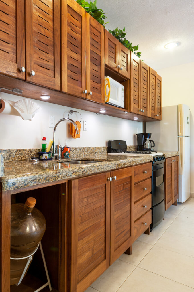 Long kitchen counter with sink beneath wooden cabinets, with a stove and refrigerator at the far end.