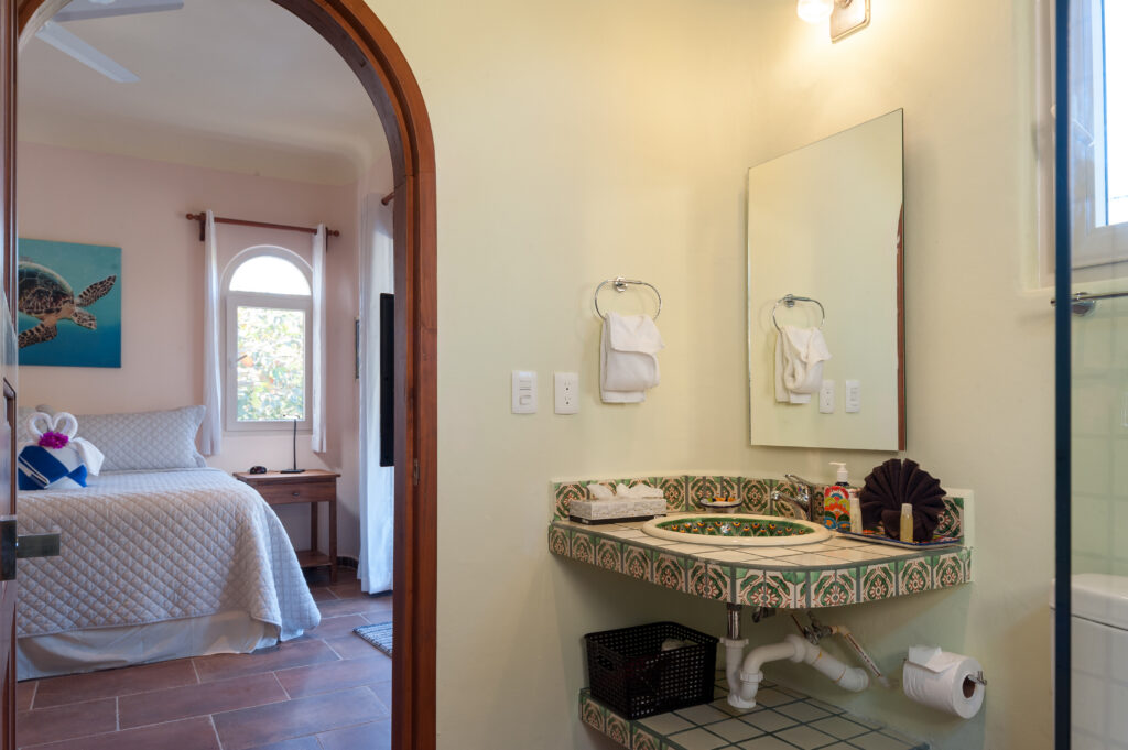 Green-patterned tiled sink beneath a mirror, with an arched doorway looking into the bedroom.