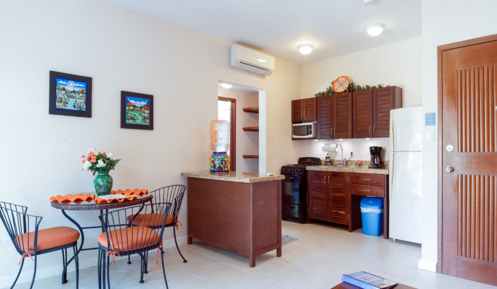 Kitchen with wooden cabinets and white refrigerator beside a round dining table and breakfast counter.