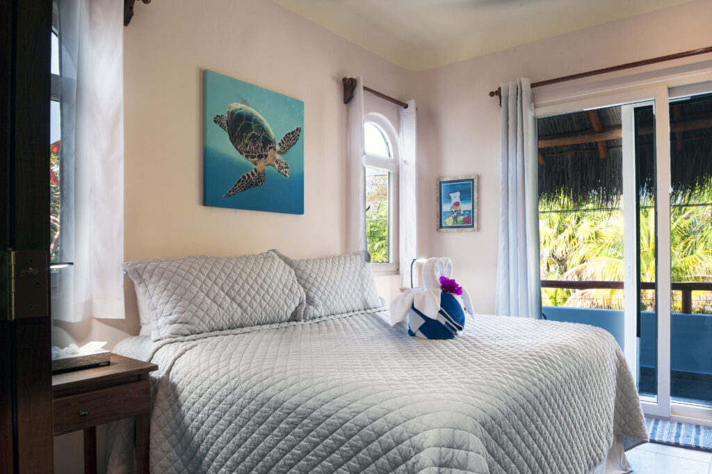 Bed with a quilted gray cover beneath turtle artwork beside sliding doors to a covered balcony.