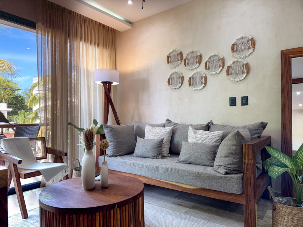 Gray sofa with patterned cushions beneath decorative wall hangings beside glass balcony doors.