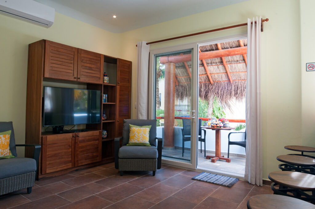Television in a tall wooden cabinet beside an armchair and glass doors to the balcony.