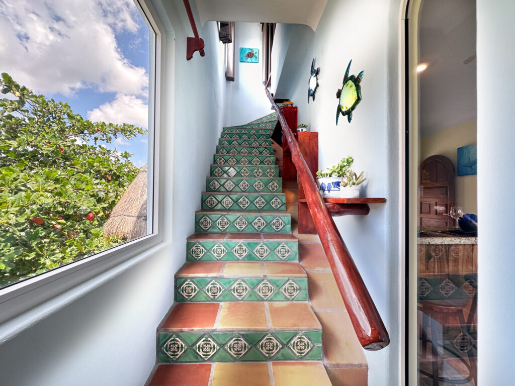 Interior stairway with patterned green tile risers, wooden handrail, and decorative wall ornaments.