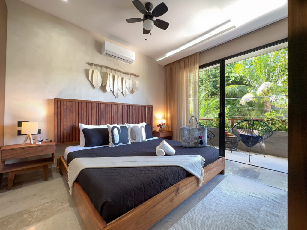 Wooden bed, matching nightstands, and ceiling fan beside a large balcony doorway.