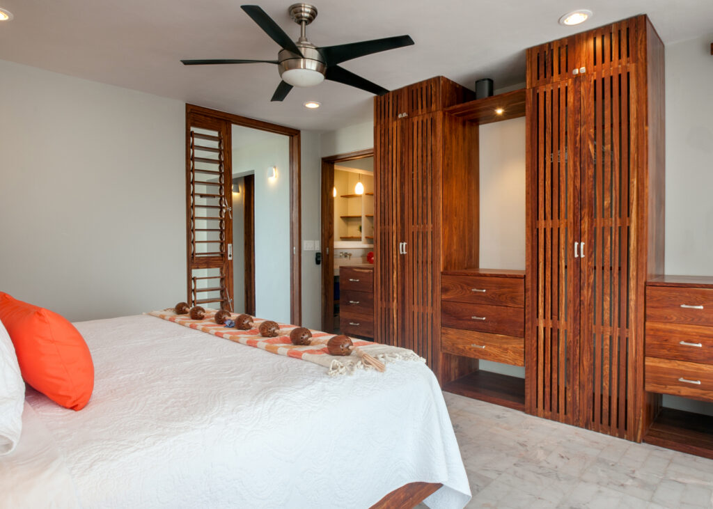 Bed with white bedding and orange pillows facing tall slatted wooden wardrobes.