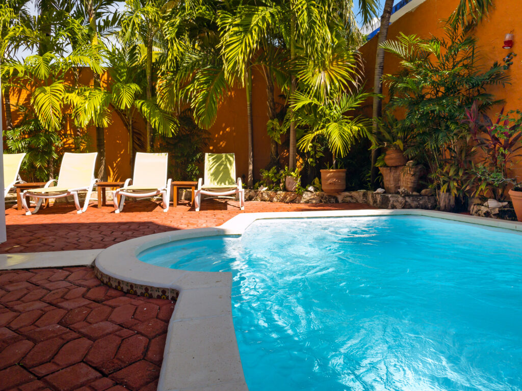 Curved blue pool surrounded by lounge chairs, palms, and orange garden walls.