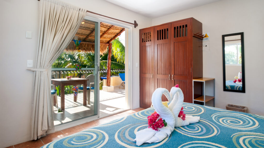 Bed with towel swans facing a wooden wardrobe and sliding doors to a terrace.