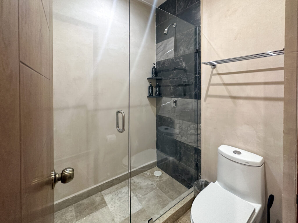 Stone-tiled shower behind glass beside a toilet and wall-mounted towel rail.