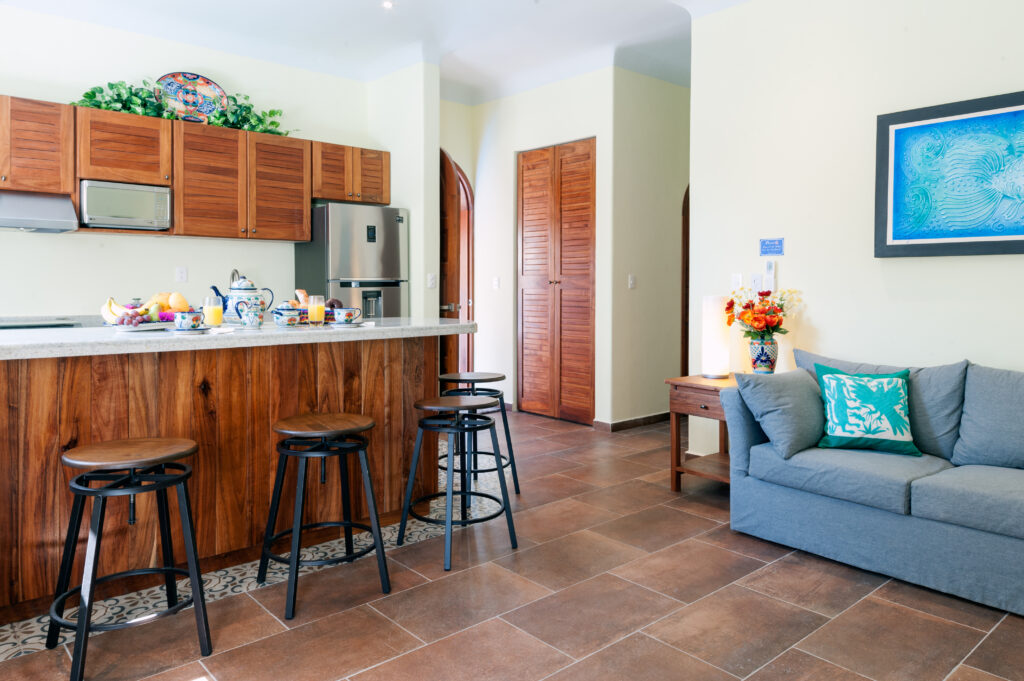 Breakfast counter with black stools beside a gray sofa and wooden storage doors.