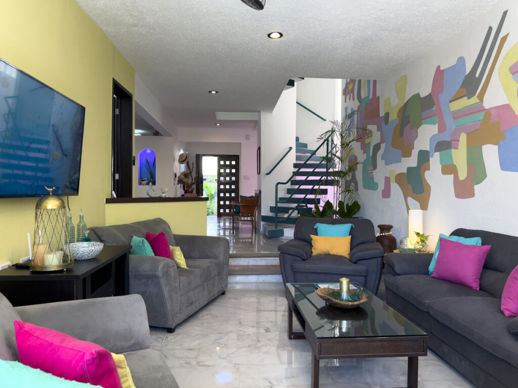 Gray sofas and armchairs with bright cushions face a glass coffee table near the staircase.