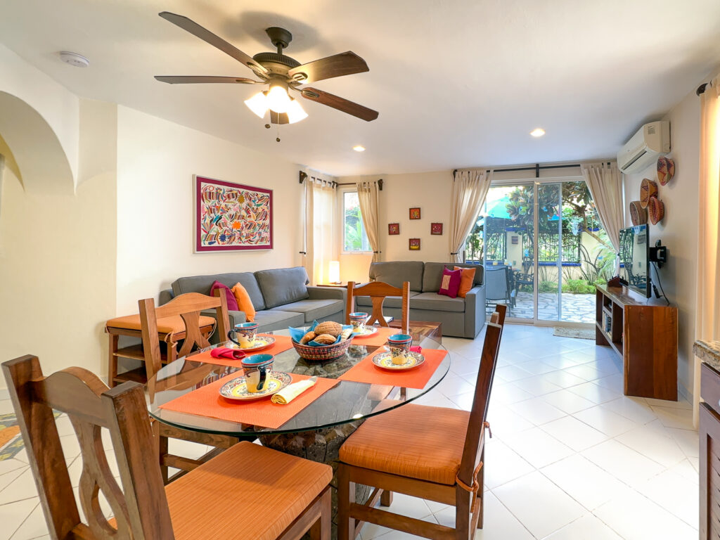 Dining table set with colorful dishes in front of two sofas and glass patio doors.
