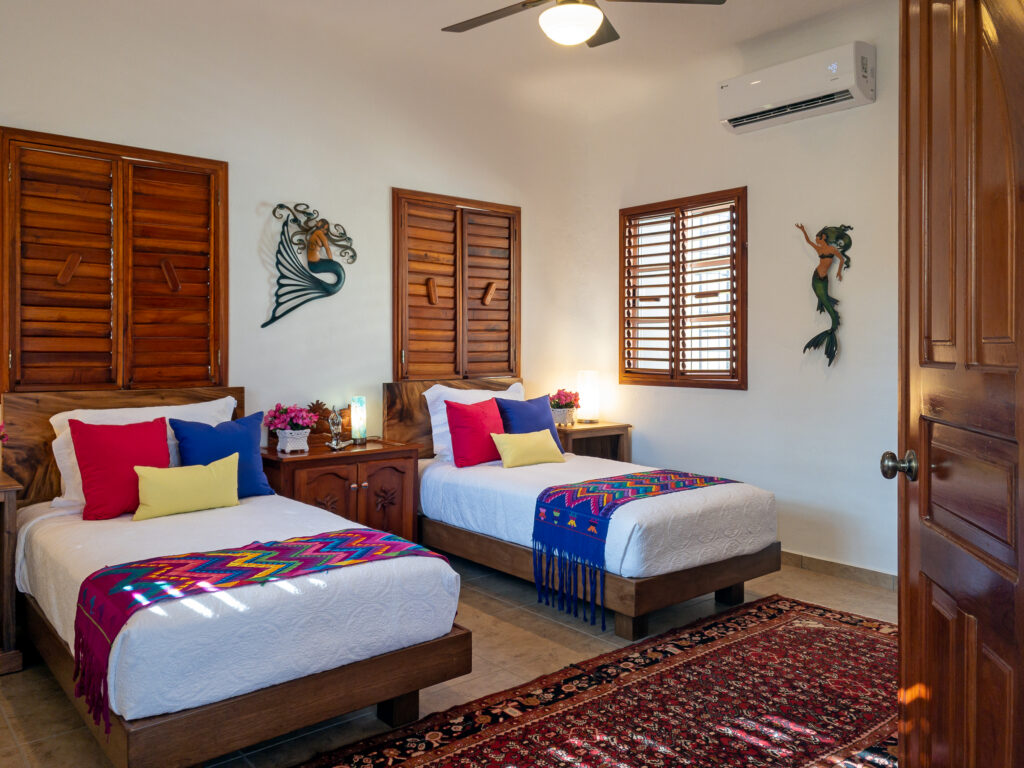 Two wooden beds with patterned runners beside matching nightstands and shuttered windows.