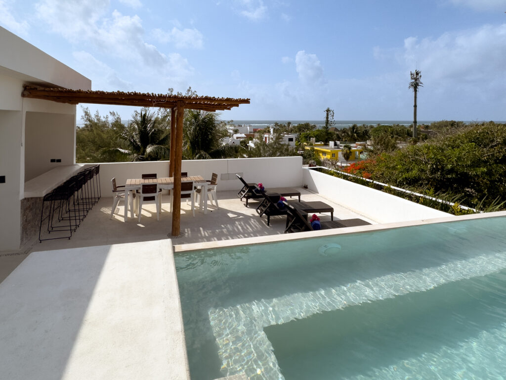 Rooftop pool beside a shaded dining area and lounge chairs overlooking treetops.