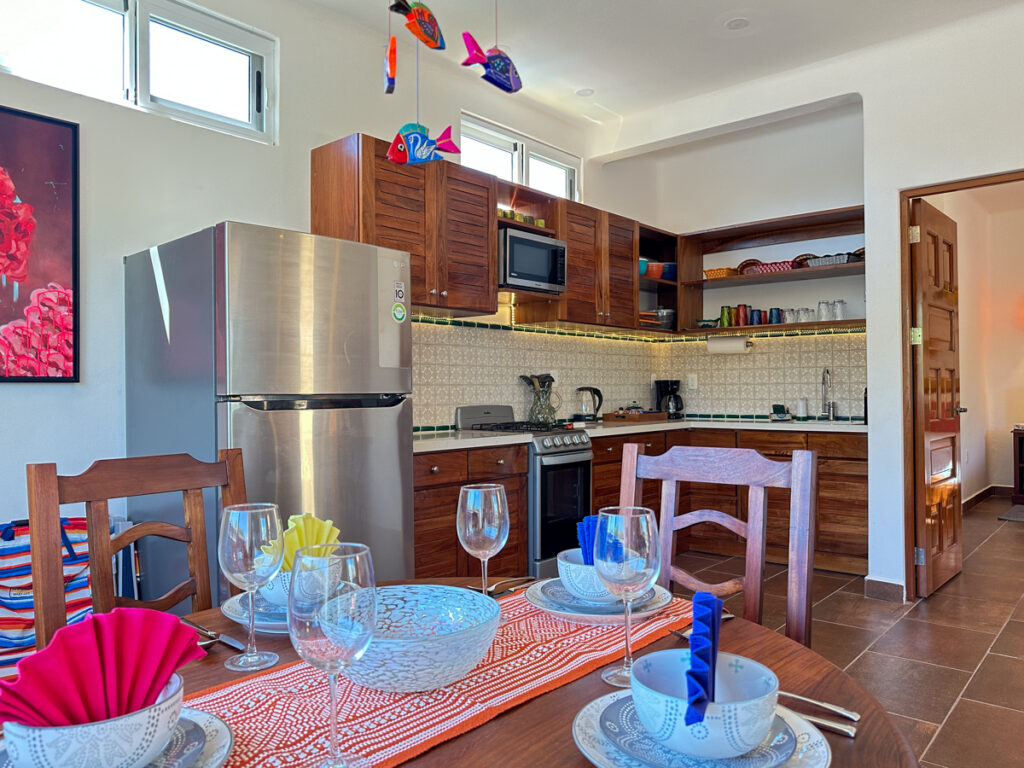Colorful place settings on a wooden dining table in front of the kitchen counter and cabinets.