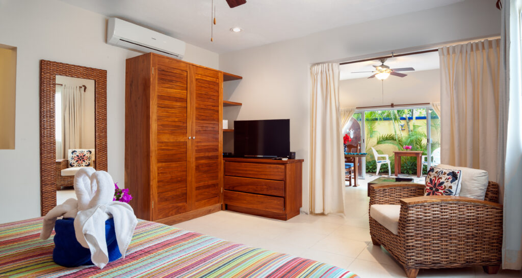 Striped bedspread beside wicker seating, a wooden wardrobe, and a dresser with a television.