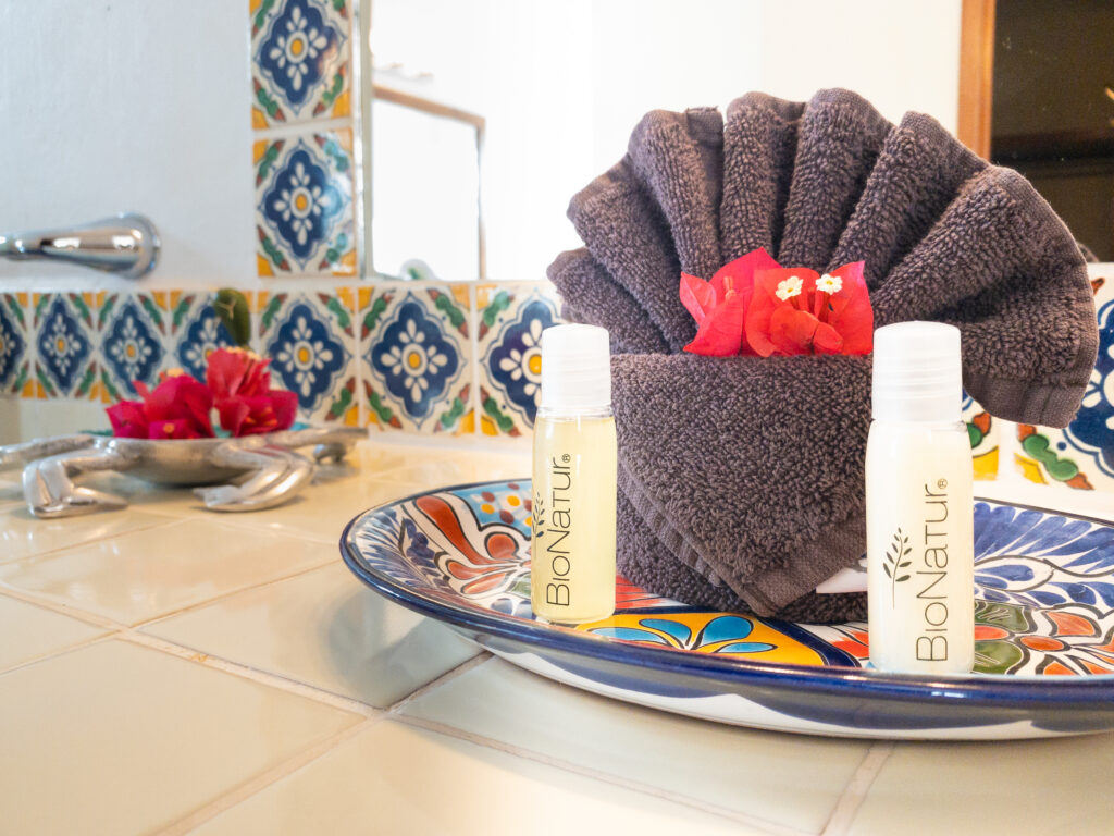 Small toiletry bottles and a folded towel with flowers on a decorative ceramic tray.