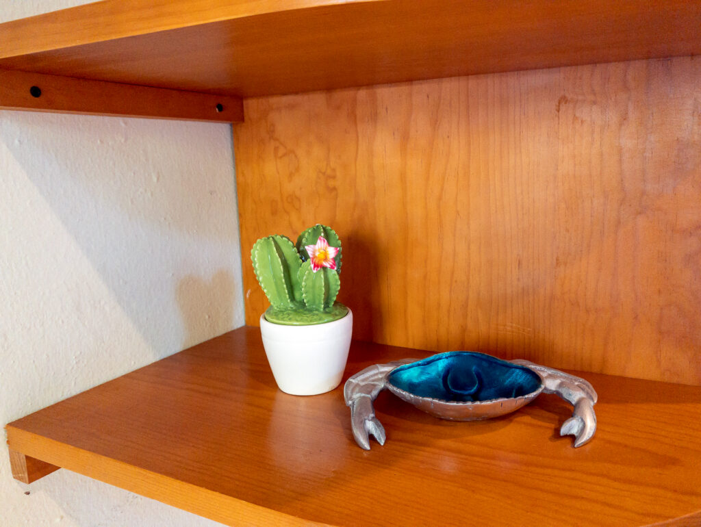 Small cactus ornament and blue crab-shaped dish on a wooden shelf.