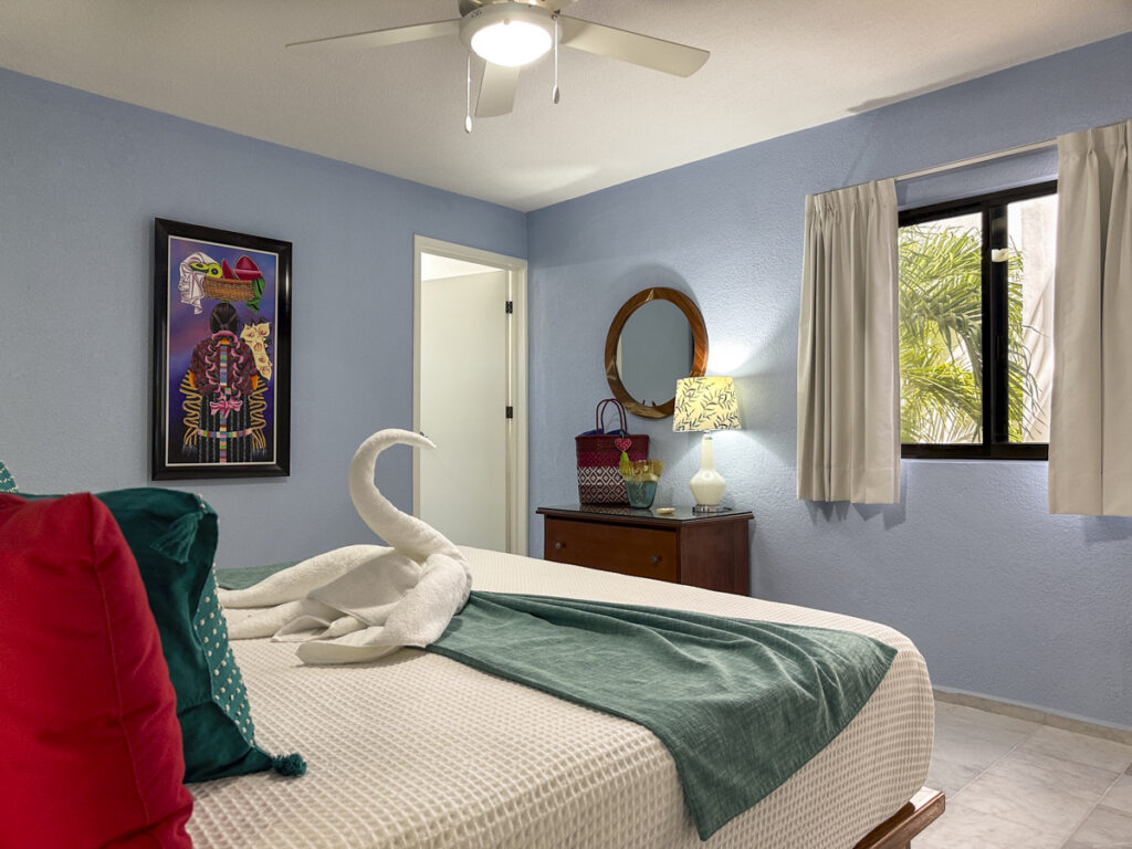 White bed with a green throw and towel swan beside a dresser in a blue bedroom.