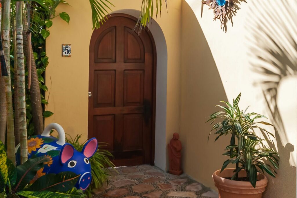 Arched wooden entrance door marked 5, surrounded by palms and potted plants.