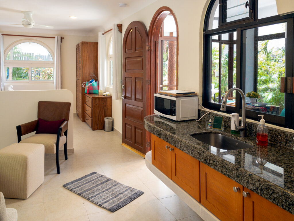 Long kitchen counter with sink and microwave beside a chair, ottoman, and arched entrance.