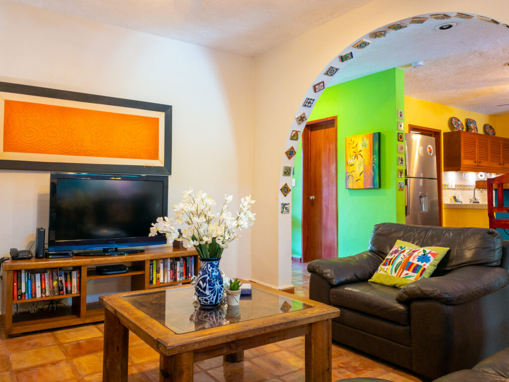 Sofa beside a wooden coffee table and television near an arched opening to the kitchen.