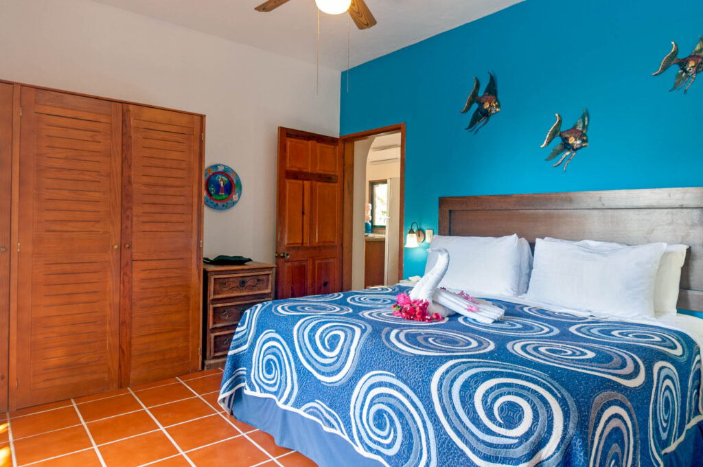 Bed with blue patterned bedding beneath bird ornaments on a bright blue wall beside wooden closets.