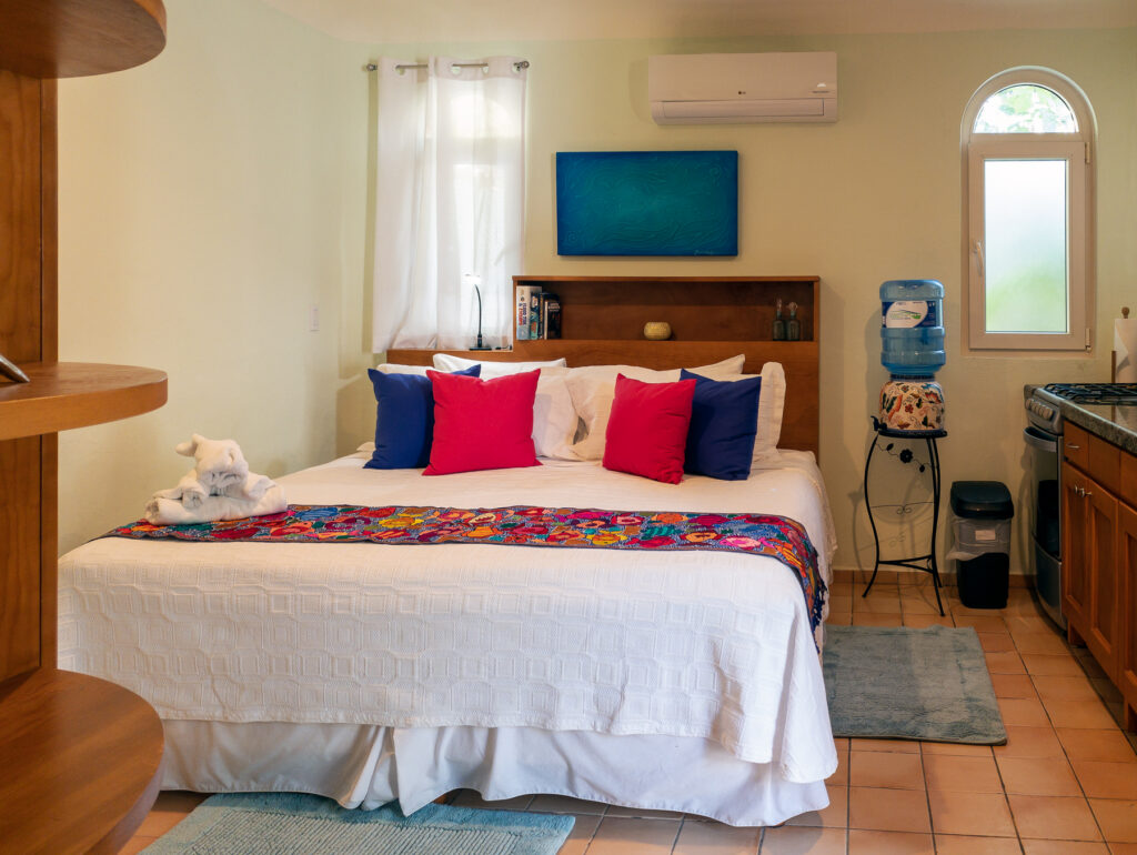 White bed with red and blue cushions and a floral runner beneath blue artwork.
