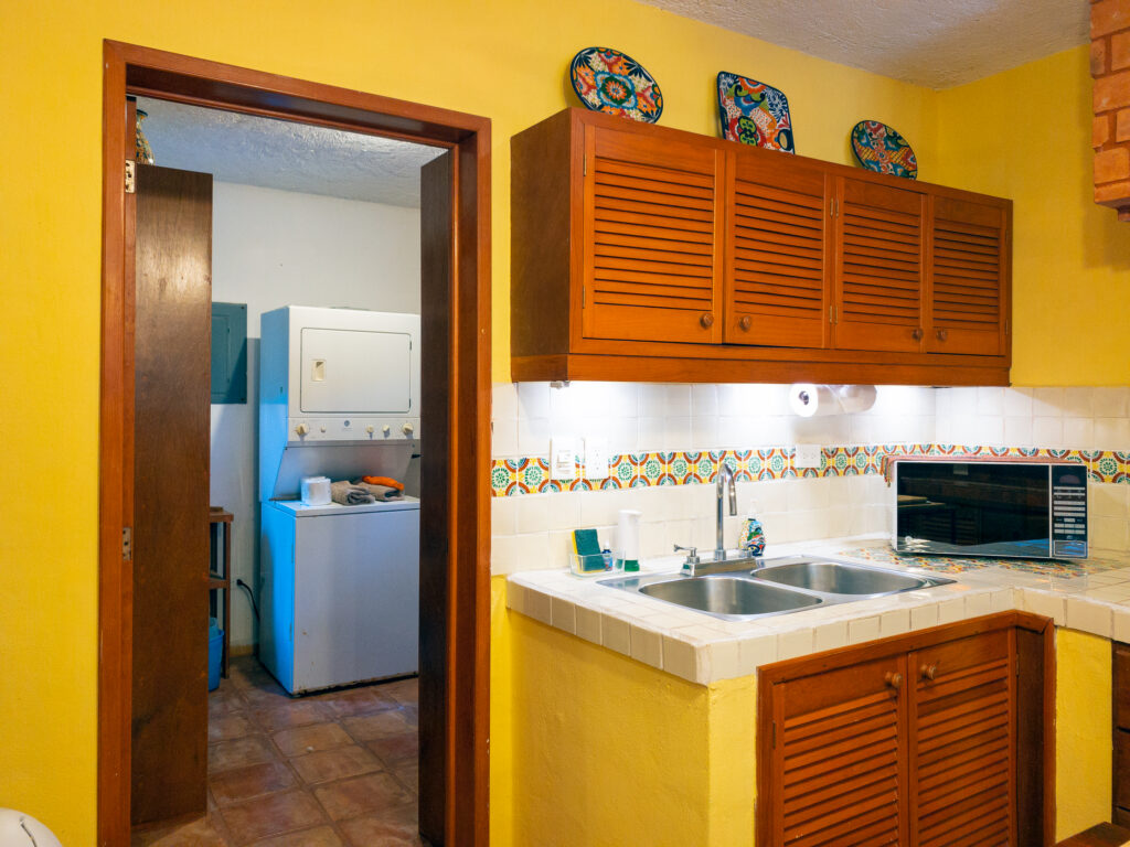 Kitchen sink and microwave beside an open doorway revealing laundry appliances.