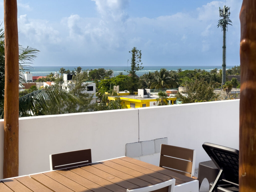 Rooftop dining table overlooking neighborhood rooftops, palms, and a distant sea horizon.