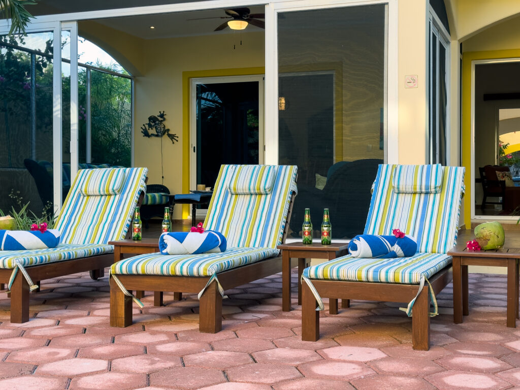 Three wooden lounge chairs with striped cushions and rolled towels outside glass patio doors.
