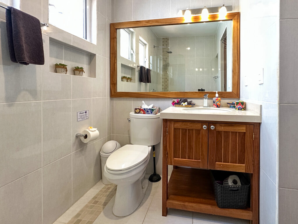 Bathroom with wooden vanity, large mirror, and toilet against pale tiled walls.