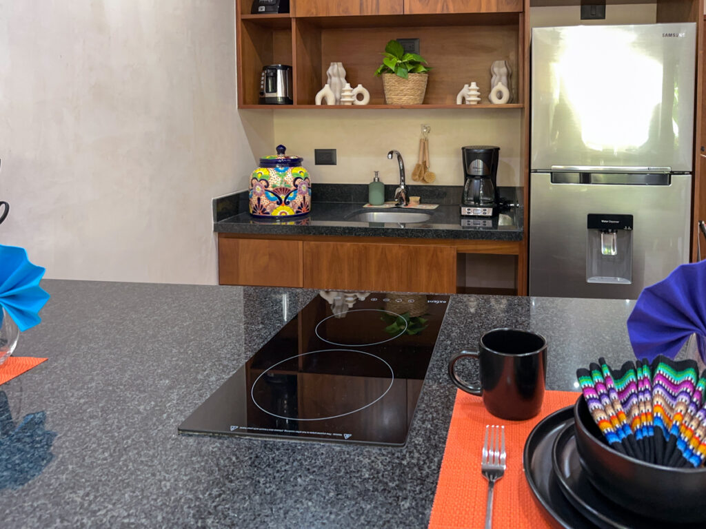 Black glass cooktop set into a dark kitchen counter beside colorful place settings.