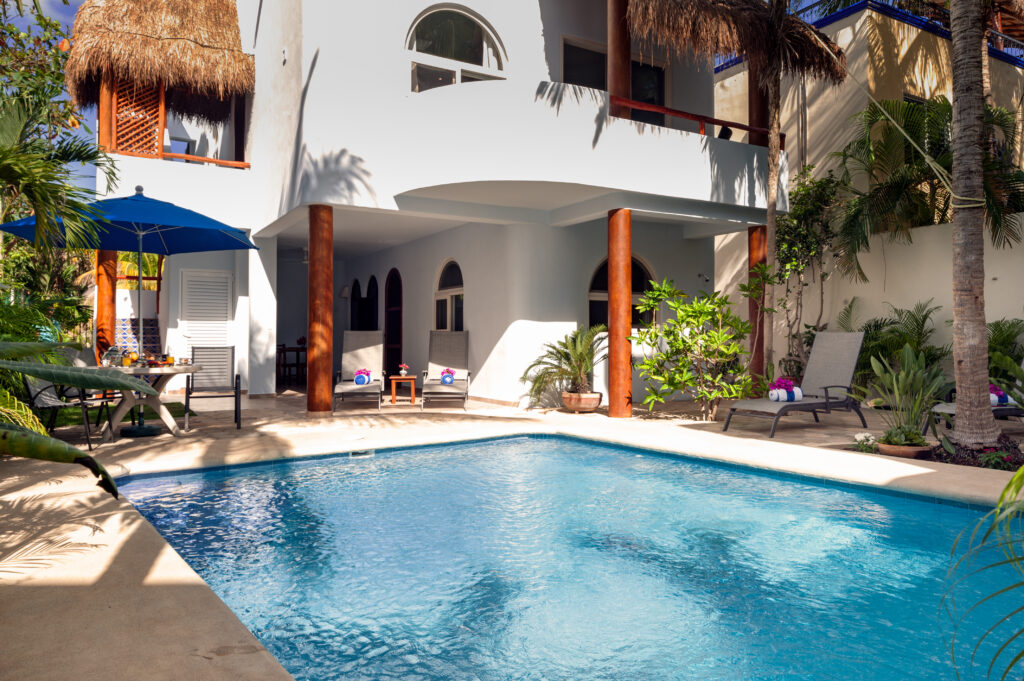 Blue pool beside a white building with arched windows, covered patios, and thatched balconies.