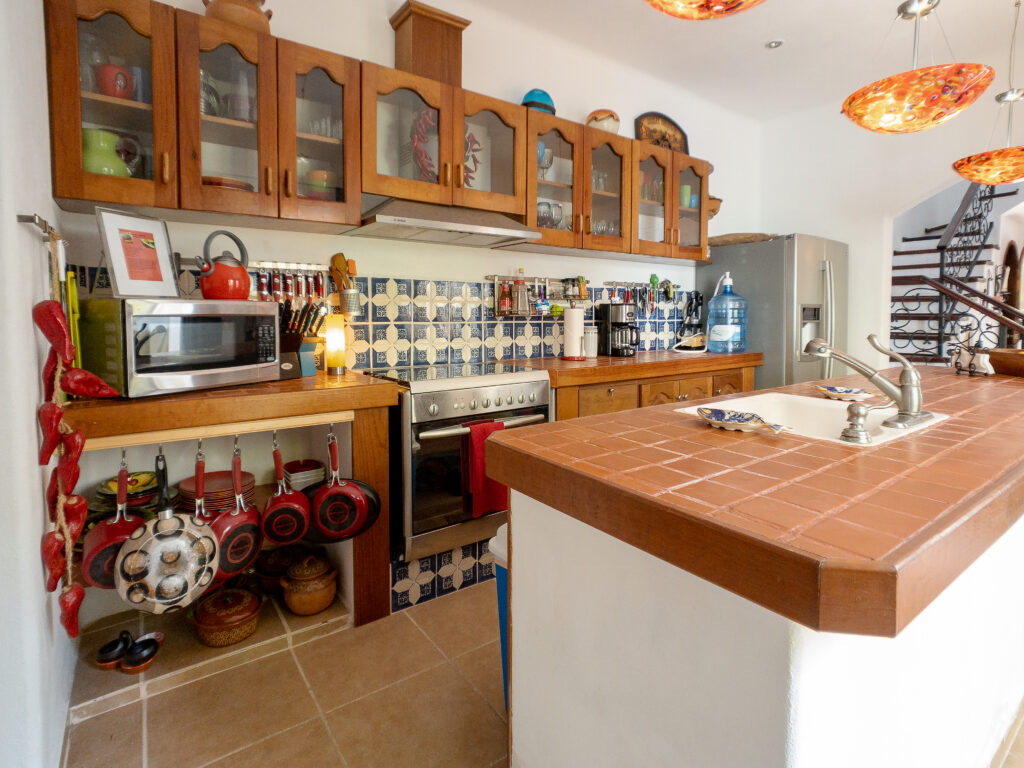 Kitchen with wooden cabinets, patterned backsplash, stove, and a large terracotta-tiled island.