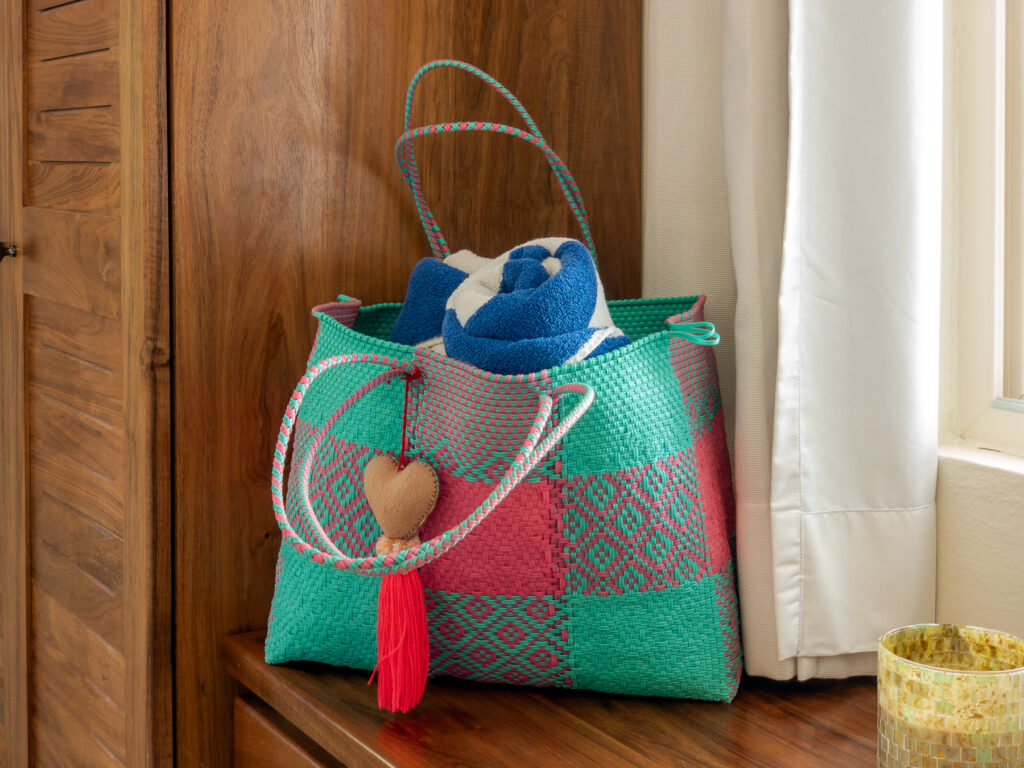 Turquoise and pink woven bag holding rolled towels on a wooden dresser.
