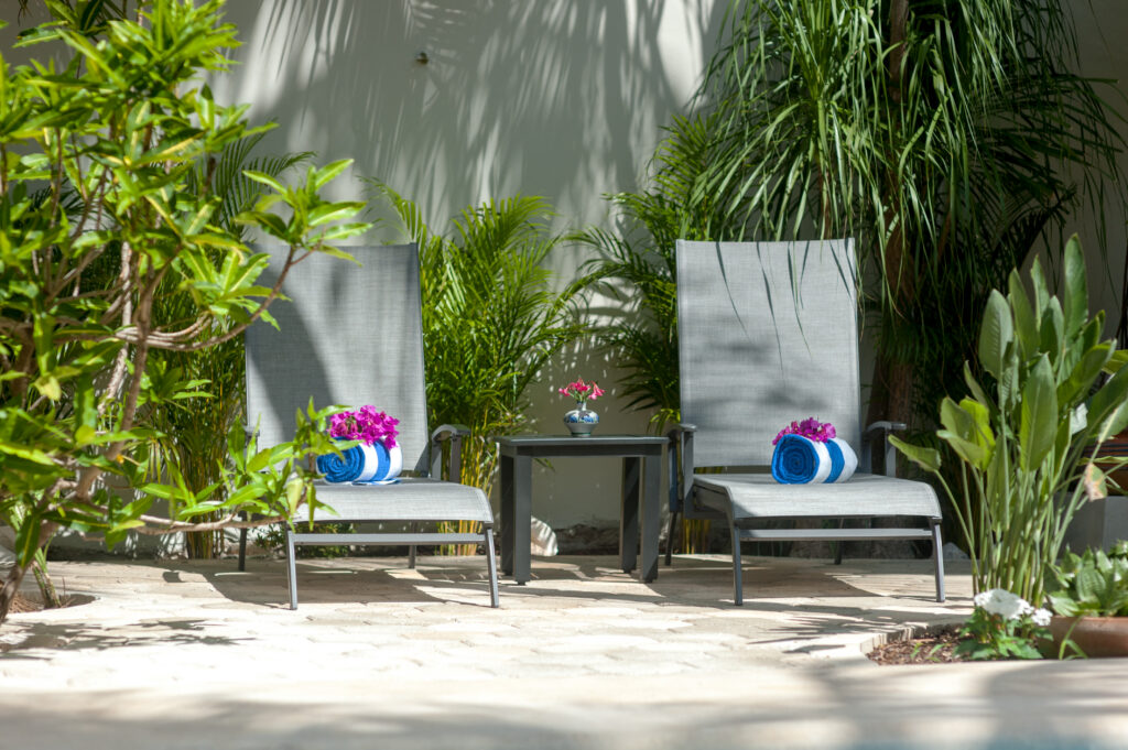 Two lounge chairs with rolled blue towels and flowers beneath dense tropical greenery.