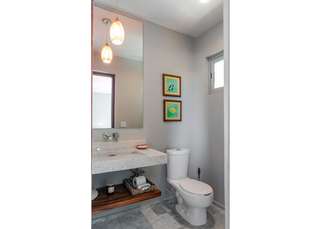 Compact bathroom with a stone sink counter, mirror, toilet, and warm pendant light.