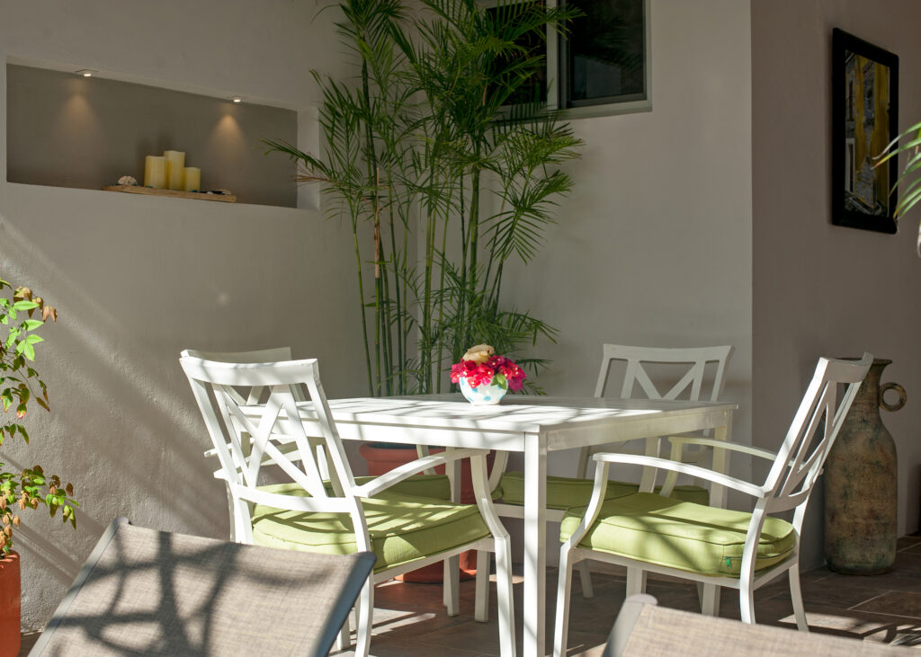 White outdoor dining set with green cushions beside palms and a vase of flowers.