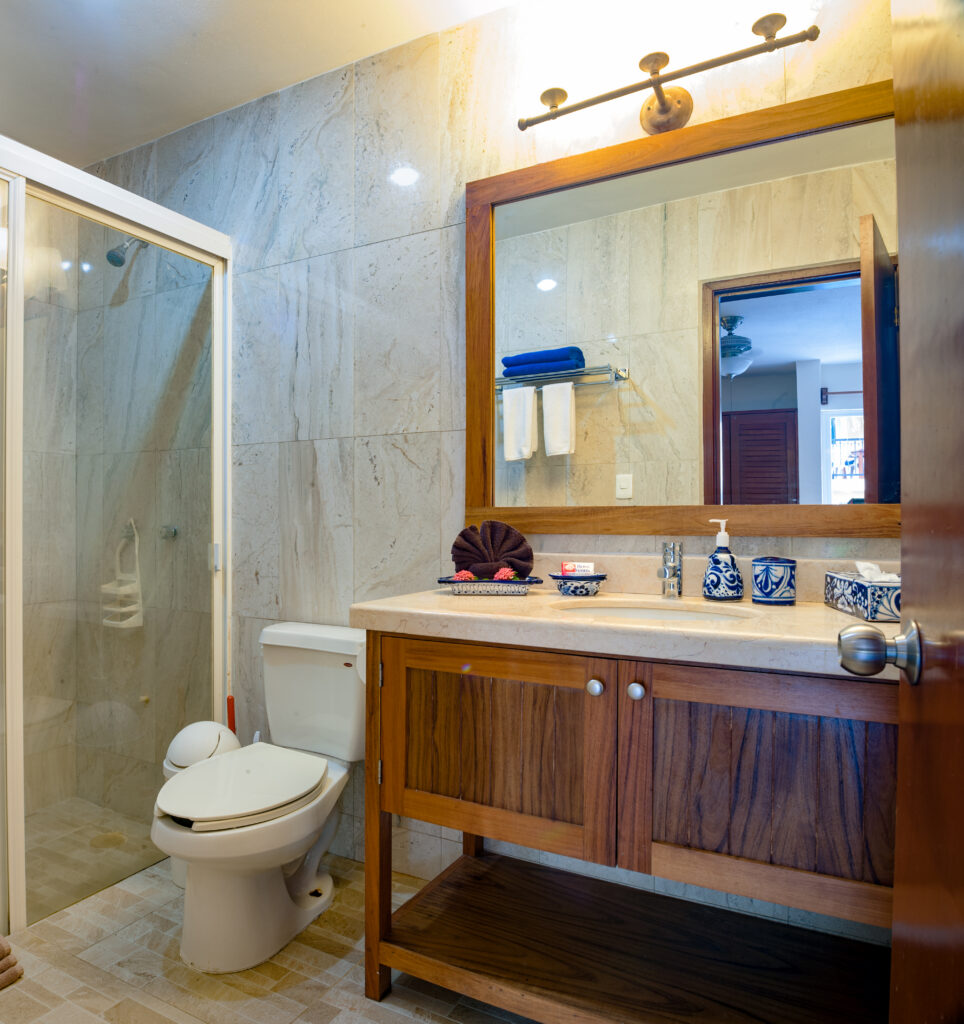 Bathroom with a wooden vanity, large mirror, toilet, and glass-enclosed shower.
