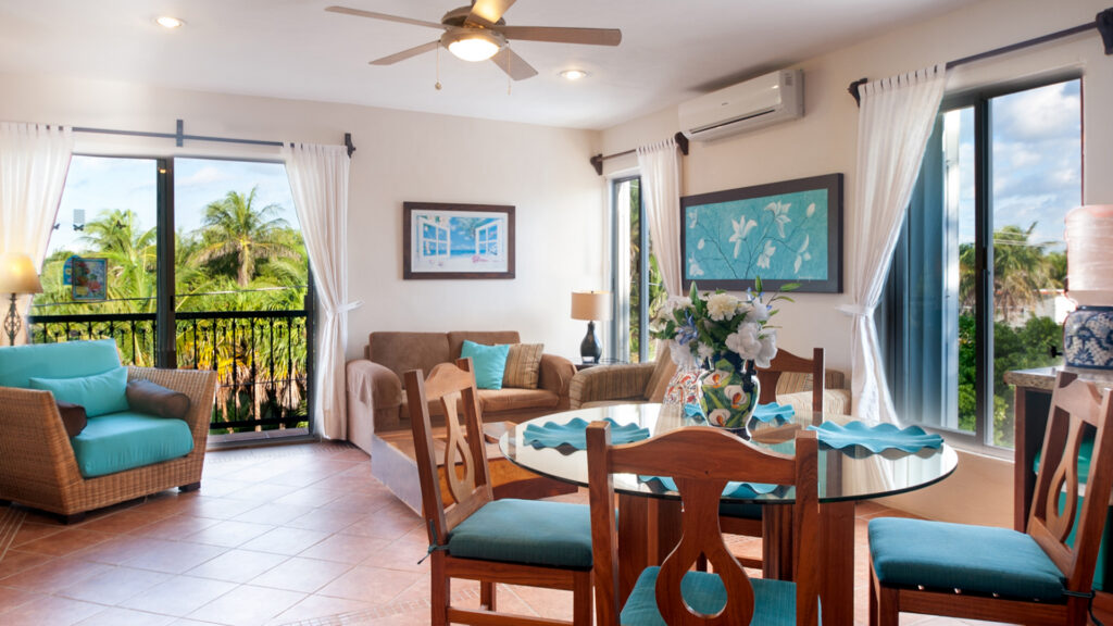 Round dining table and wicker seating beside sliding balcony doors overlooking palms.